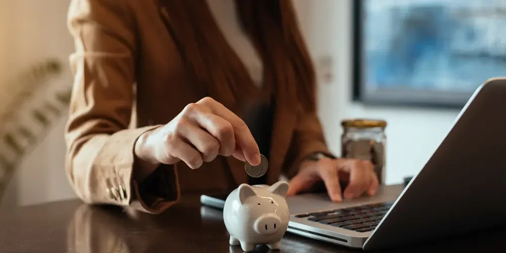 mUJER DEPOSITANDO MONEDAS EN UN VASO DE VIDRIO